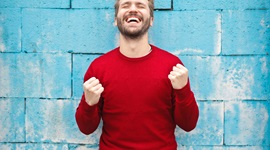 Man in red jumper fist pumping with eyes closed and a huge smile on his face