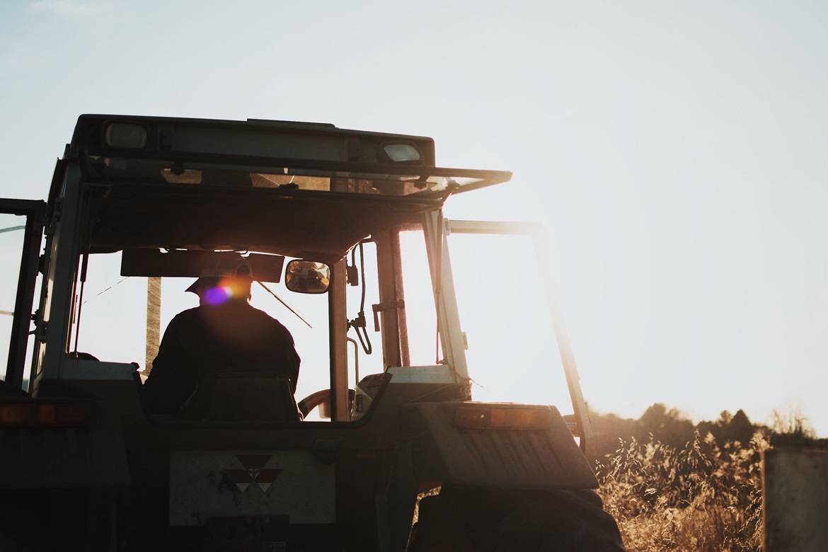 Person in tractor with sun setting in background