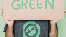 Person wearing a tshirt with a recycling symbol around the world holding a sign reading Go Green in front of face