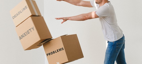 Man pushing over a pile of cardboard boxes each with one of these words on: problems, anxiety, break up, workload, deadline and stress.