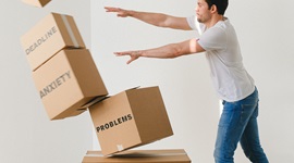 Man pushing over a pile of cardboard boxes each with one of these words on: problems, anxiety, break up, workload, deadline and stress.