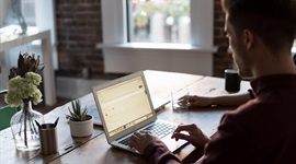 Photo of man sat at a desk on an apple mac laptop