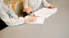 2 women talking at a desk over pages of notes.