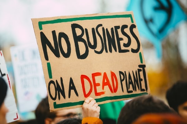 Sign reading 'No Business on a Dead Planet' being held up within a crowd.