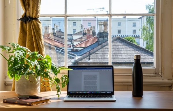 photo-1591382696448-3809bb398c0e Laptop placed on a desk by a window, overlooking rows of houses.