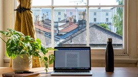 Laptop placed on a desk by a window, overlooking rows of houses.