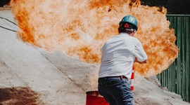 Man in safety hat holding fire extinguisher putting out a fire in an oil drum