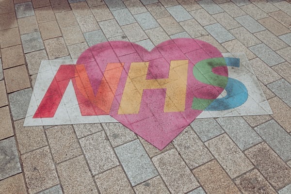 photo-1594760394382-150da4d8c2b1 Street art showing the NHS logo in colours and on a heart background.