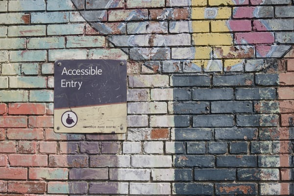 photo-1600202751116-3e0226e1e7a0 Brick wall with sign reading 'Accessible Entry'.
